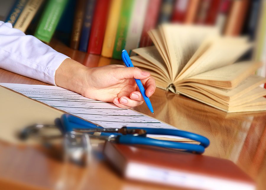 A Legal Nurse Consultant's hand writing on a piece of paper with a stethoscope.