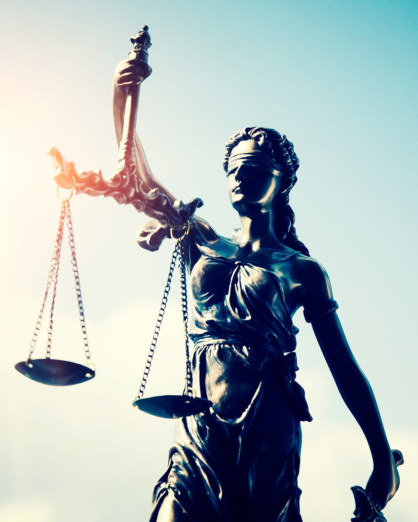 Bronze statue of Lady Justice holding scales and a sword, with a blindfold over her eyes, set against a blue sky background.